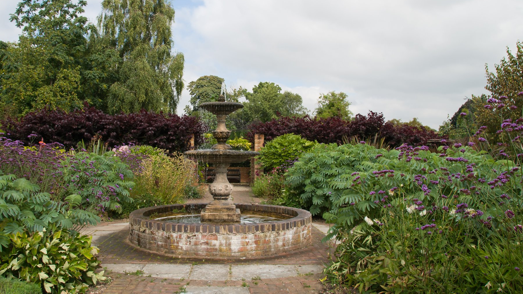 There is a fountain in the middle of a garden surrounded by flowers.
