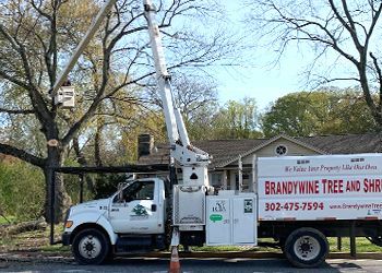 A white truck with a crane attached to it is parked in front of a house.