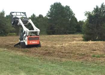 A bobcat is cutting grass in a field.