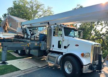 A white truck with a crane attached to it is parked in front of a house.