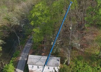 An aerial view of a house with a crane cutting a tree.