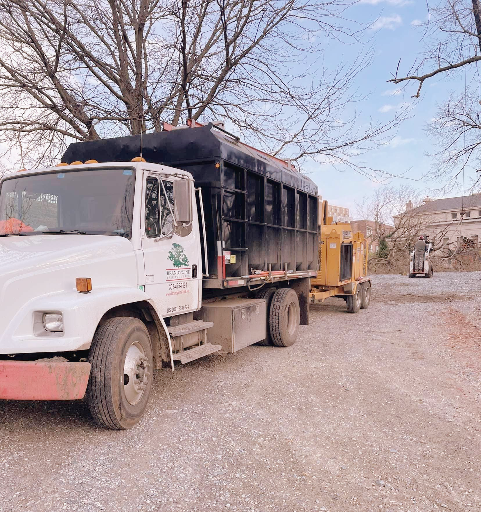 A white truck is parked in a gravel lot next to a yellow truck.