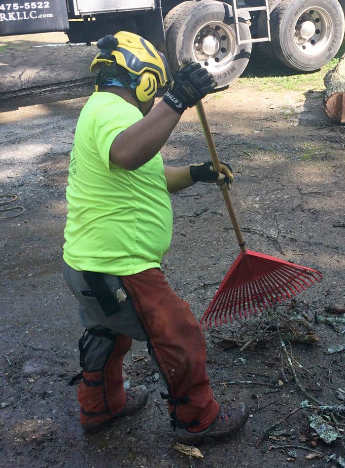 A man wearing a yellow helmet is holding a red rake