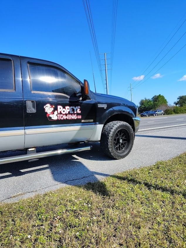 Black and silver Popeye Towing truck parked on the side of a road, bright sunny day.