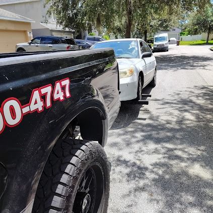 Tow truck towing a white car on a sunny street.