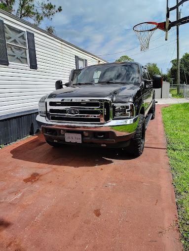 Black pickup truck parked in a driveway next to a white house with a basketball hoop.