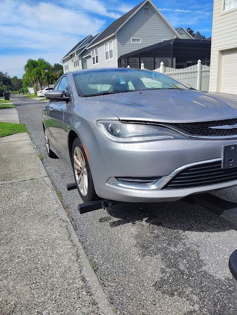 Silver Chrysler sedan parked on a driveway, front tire on a black ramp. Sunny day.