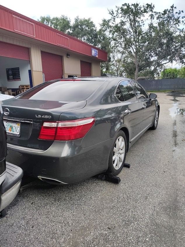Dark gray Lexus LS 460 parked outside a building with red and beige trim, a wet parking lot.