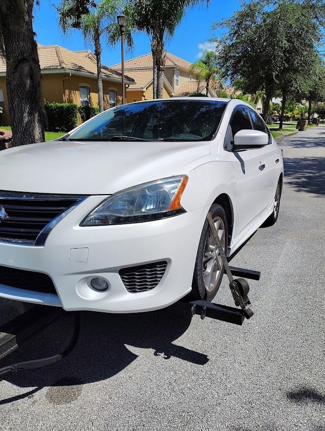 White Nissan sedan on a tow dolly parked on a residential street.