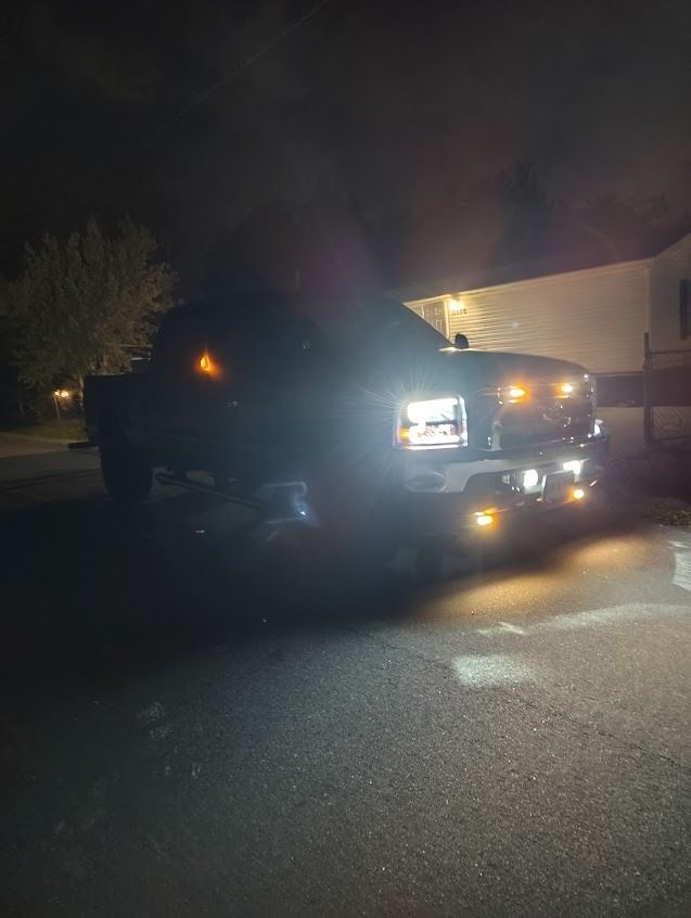 A black pickup truck with bright headlights and amber lights on at night.