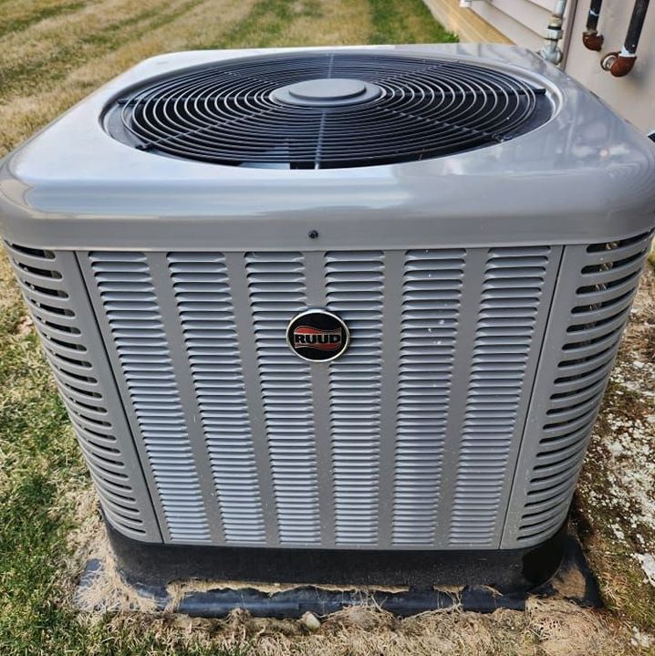 A large gray RUUD air conditioner is sitting outside of a building.