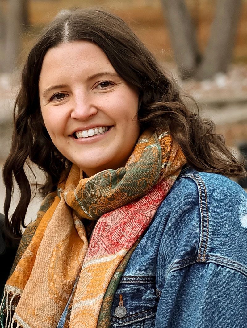A woman wearing a scarf and a denim jacket is smiling for the camera.