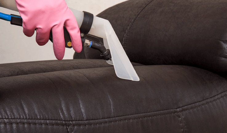 A woman is cleaning a couch with a vacuum cleaner.