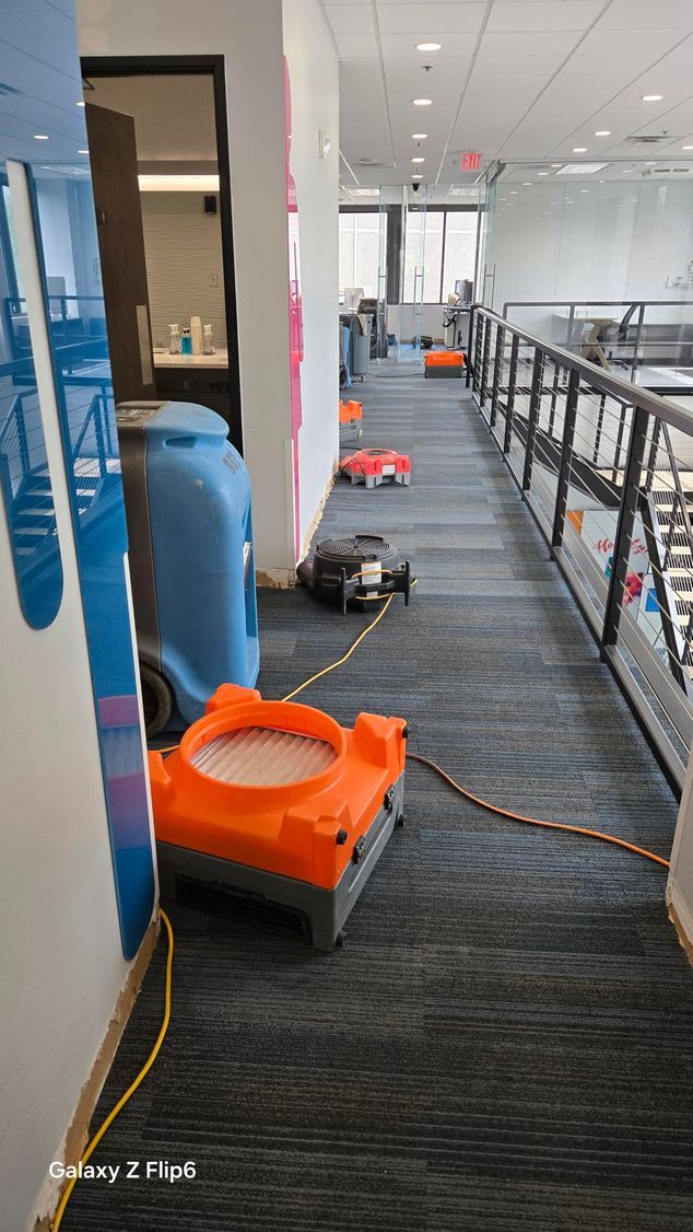 A man and a boy are sitting on a couch in a living room with a bucket of water on the floor.