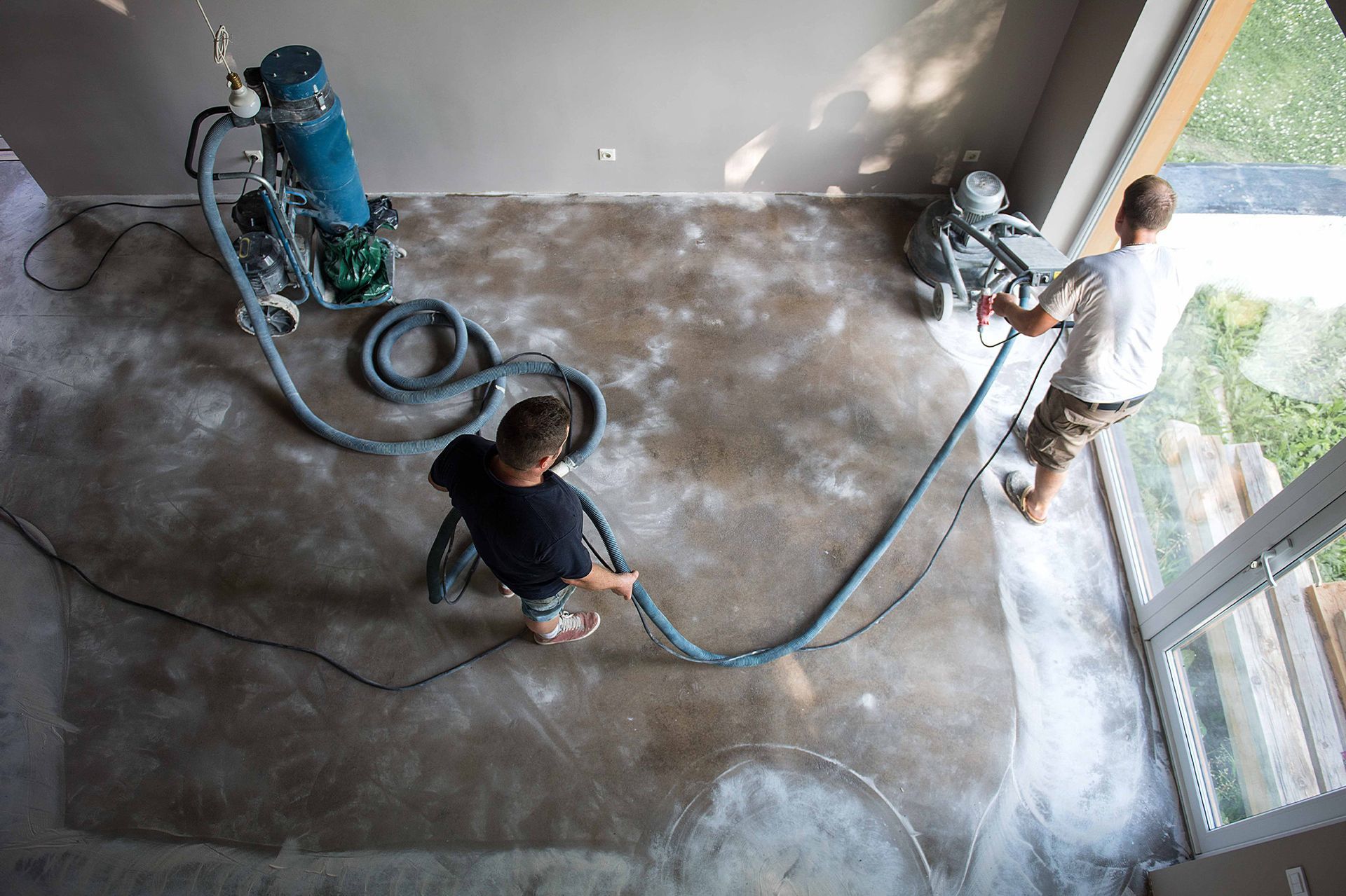 Two men are working on a concrete floor with a vacuum cleaner.