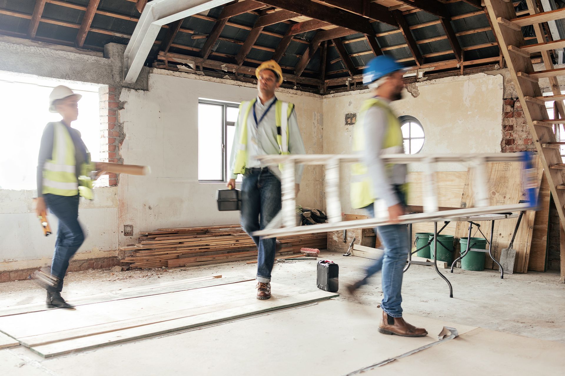 A group of construction workers are carrying a ladder in a building under construction.
