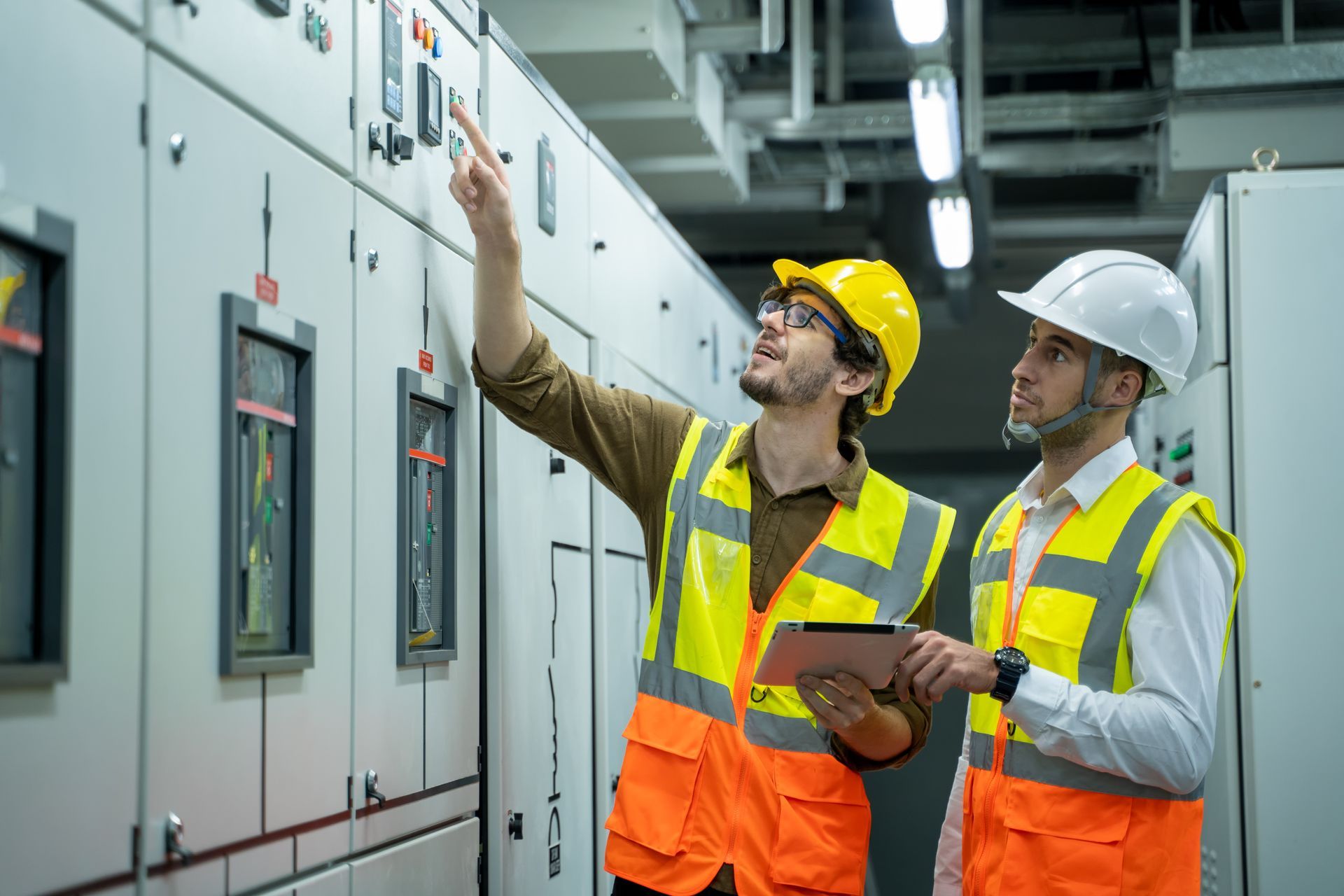 Two electrical engineers are looking at a control panel in a factory.