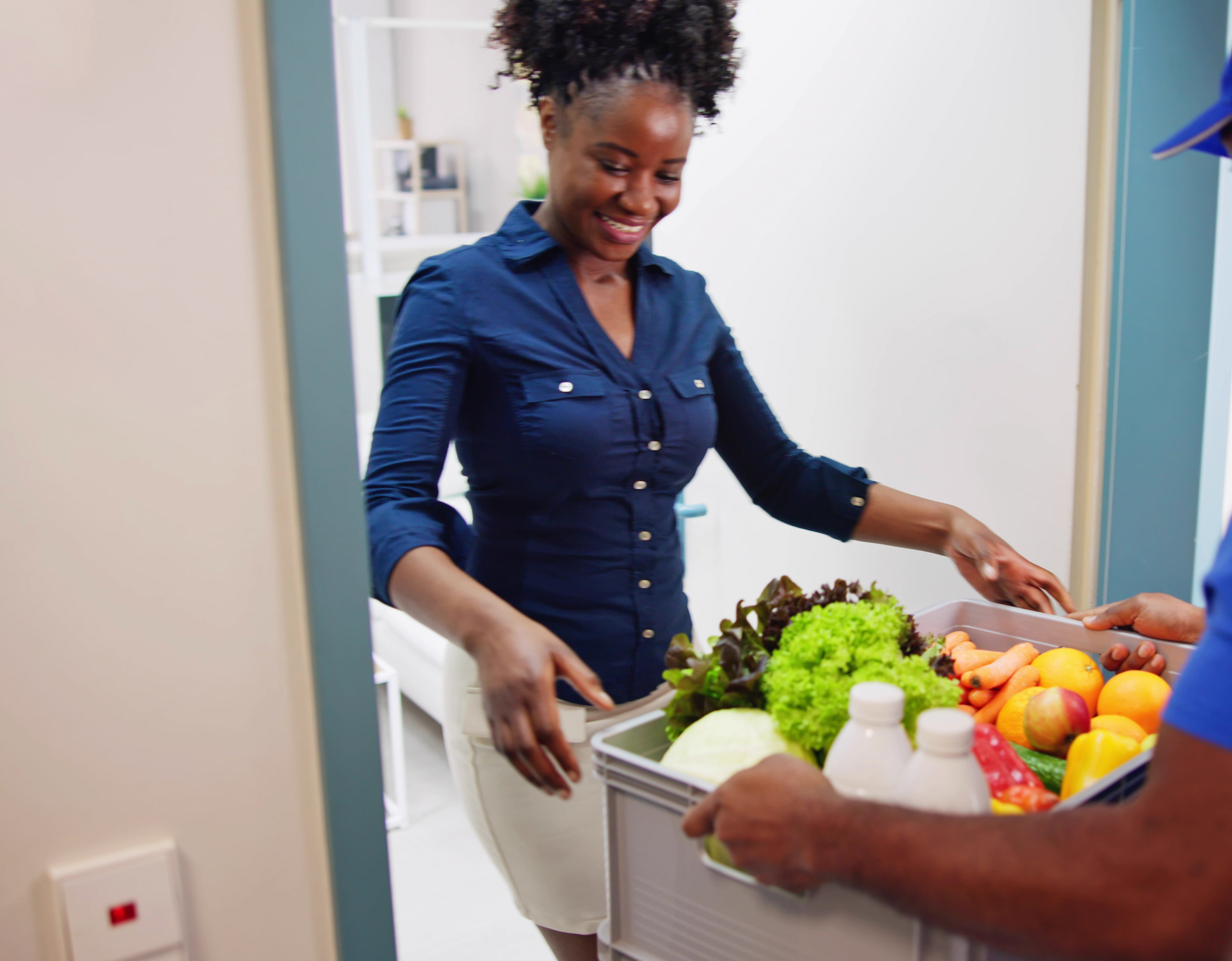 A woman is getting a box of fruits and vegetables from a delivery man.