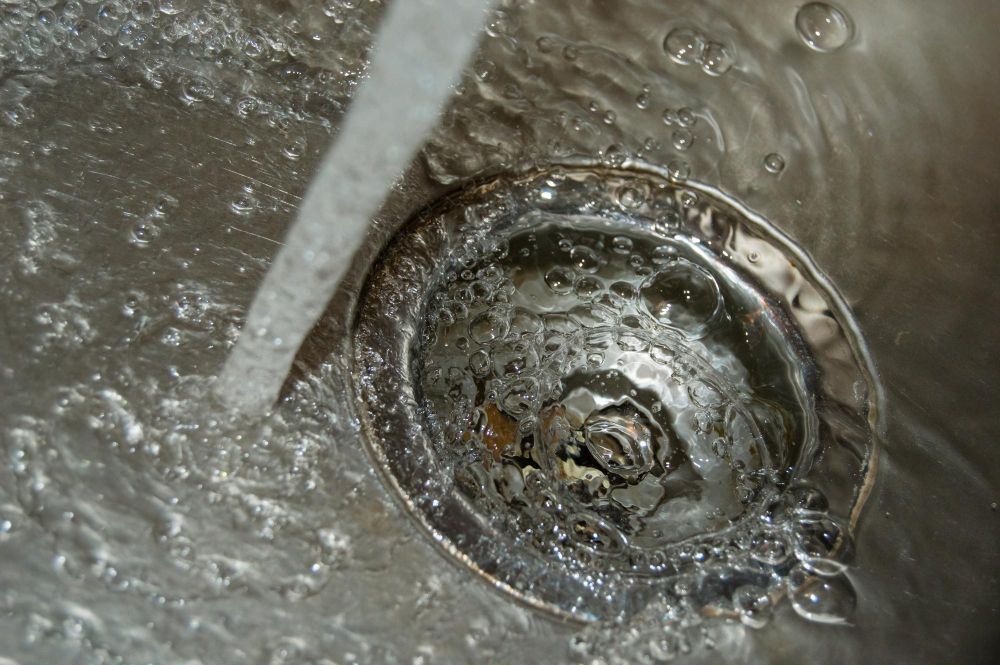 Water flowing into a stainless steel sink, over a drain.