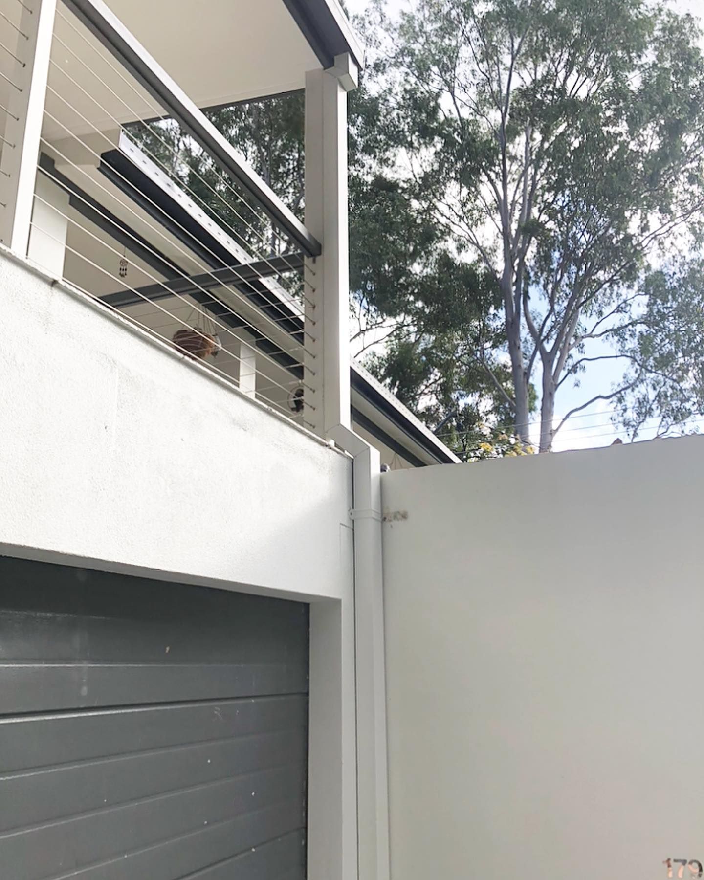 White exterior wall with gray garage door, railing, and a section of white gate.