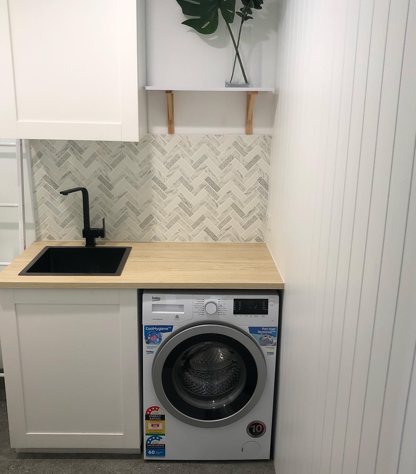 Laundry room with washing machine, sink, white cabinets, and herringbone backsplash.