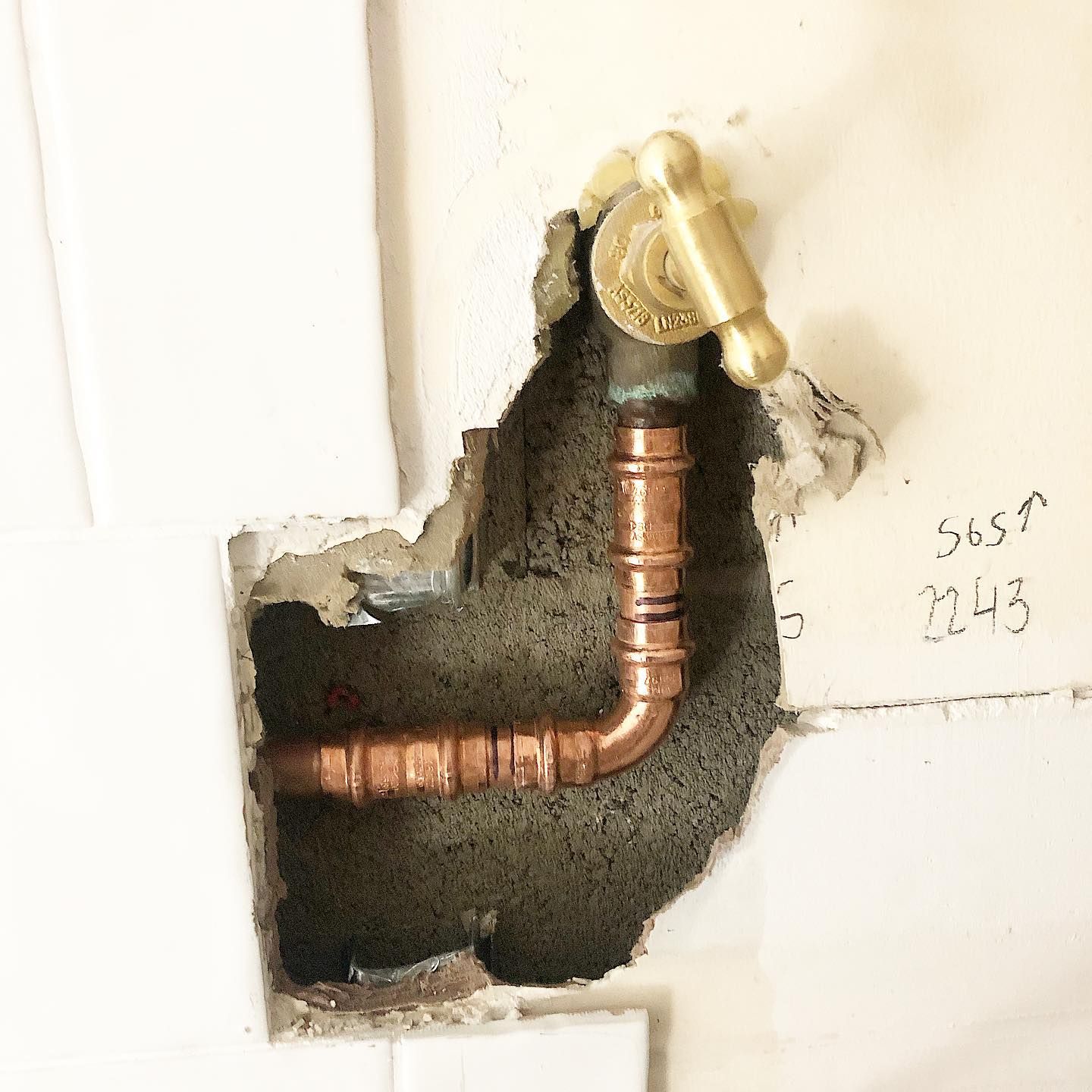 Copper plumbing pipes and valve protruding from a hole in a white wall.