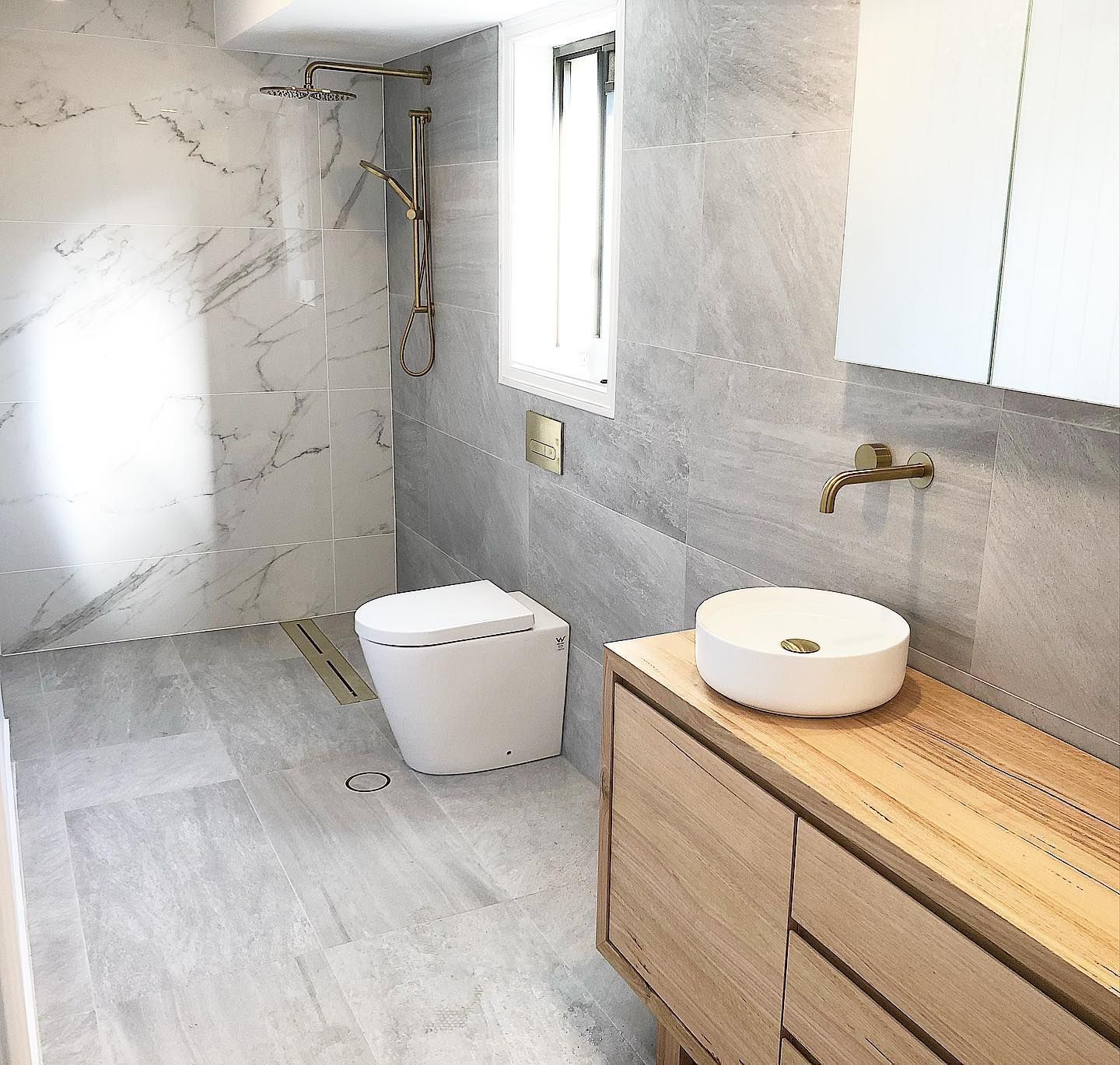 Modern bathroom with gray tile, wood vanity, and gold fixtures.