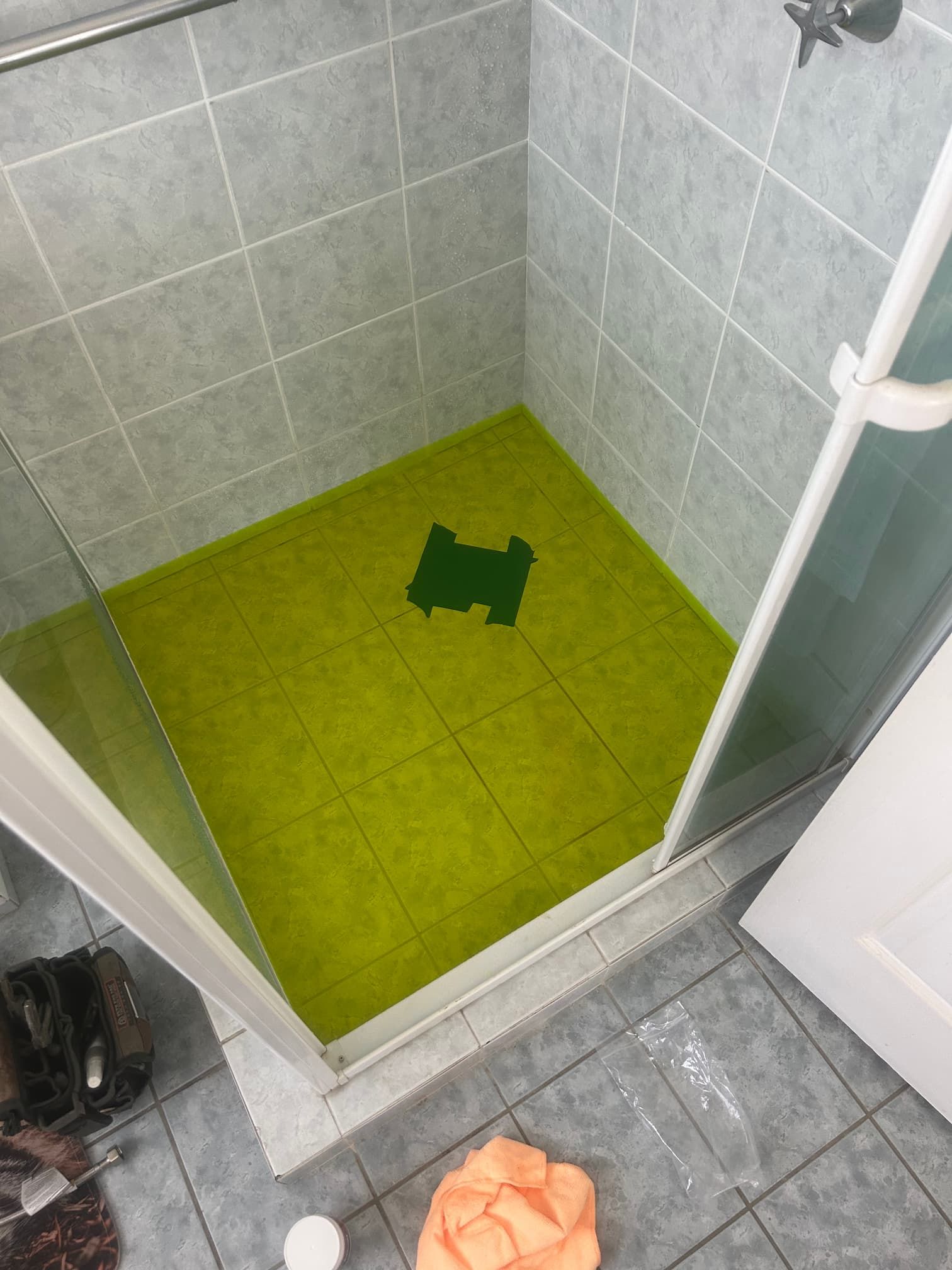 Shower with green floor covering and grey tiled walls.