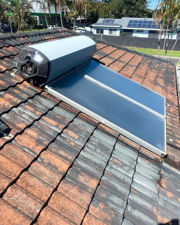 Solar water heater installed on a tiled rooftop. A rectangular panel and cylindrical tank are visible.