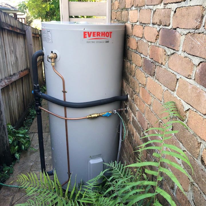 Electric water heater next to a brick wall and wooden fence, with surrounding plants.