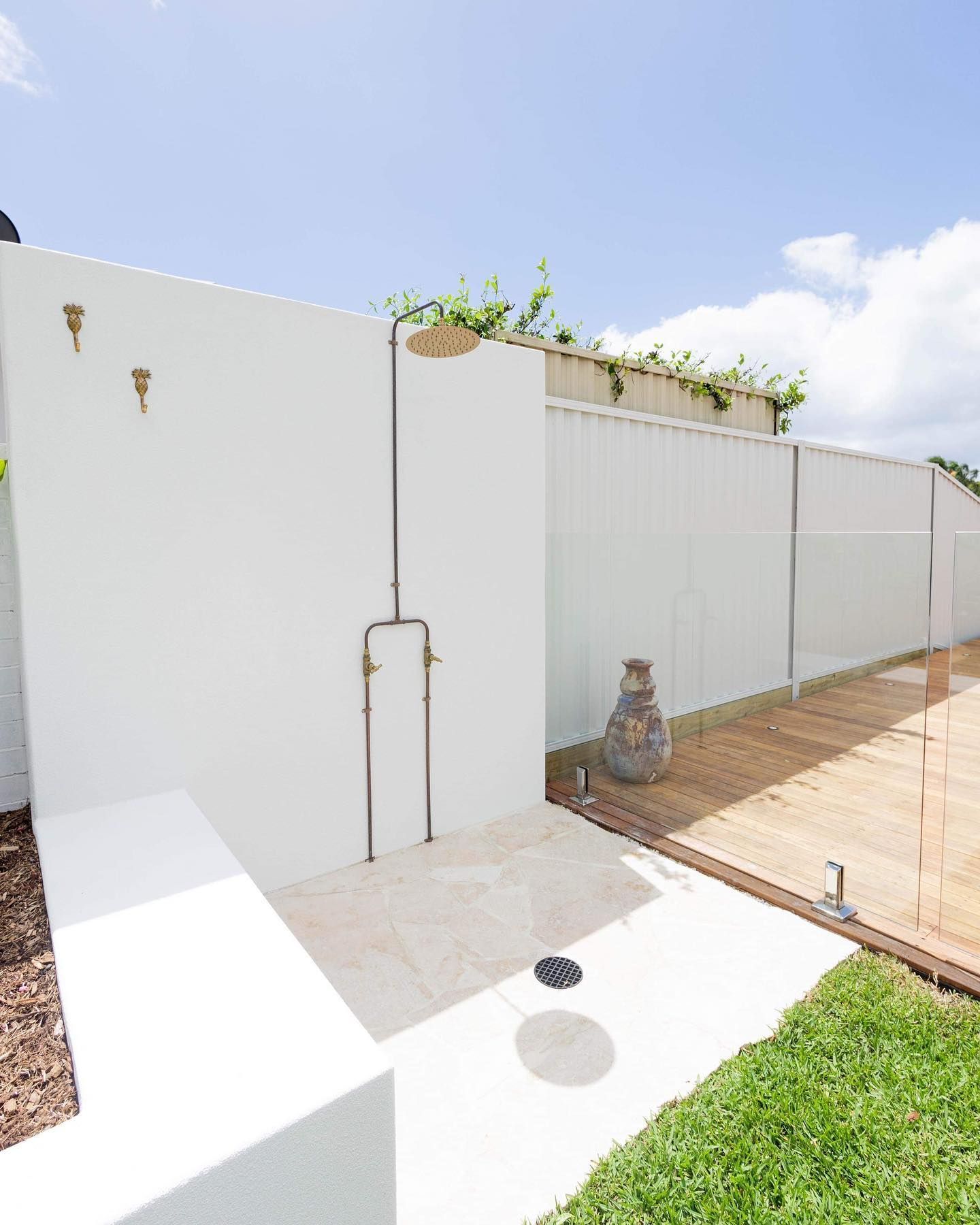 Outdoor shower head with water cascading down, surrounded by green foliage.