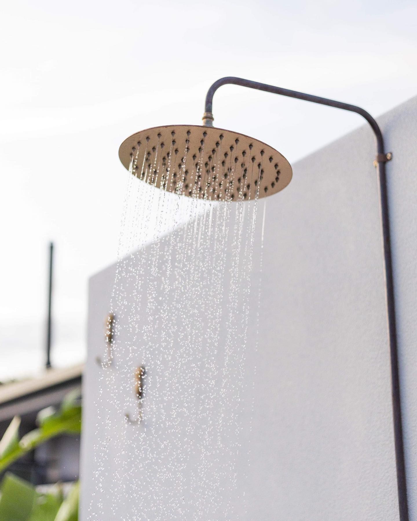 Outdoor shower head spraying water onto a white wall.
