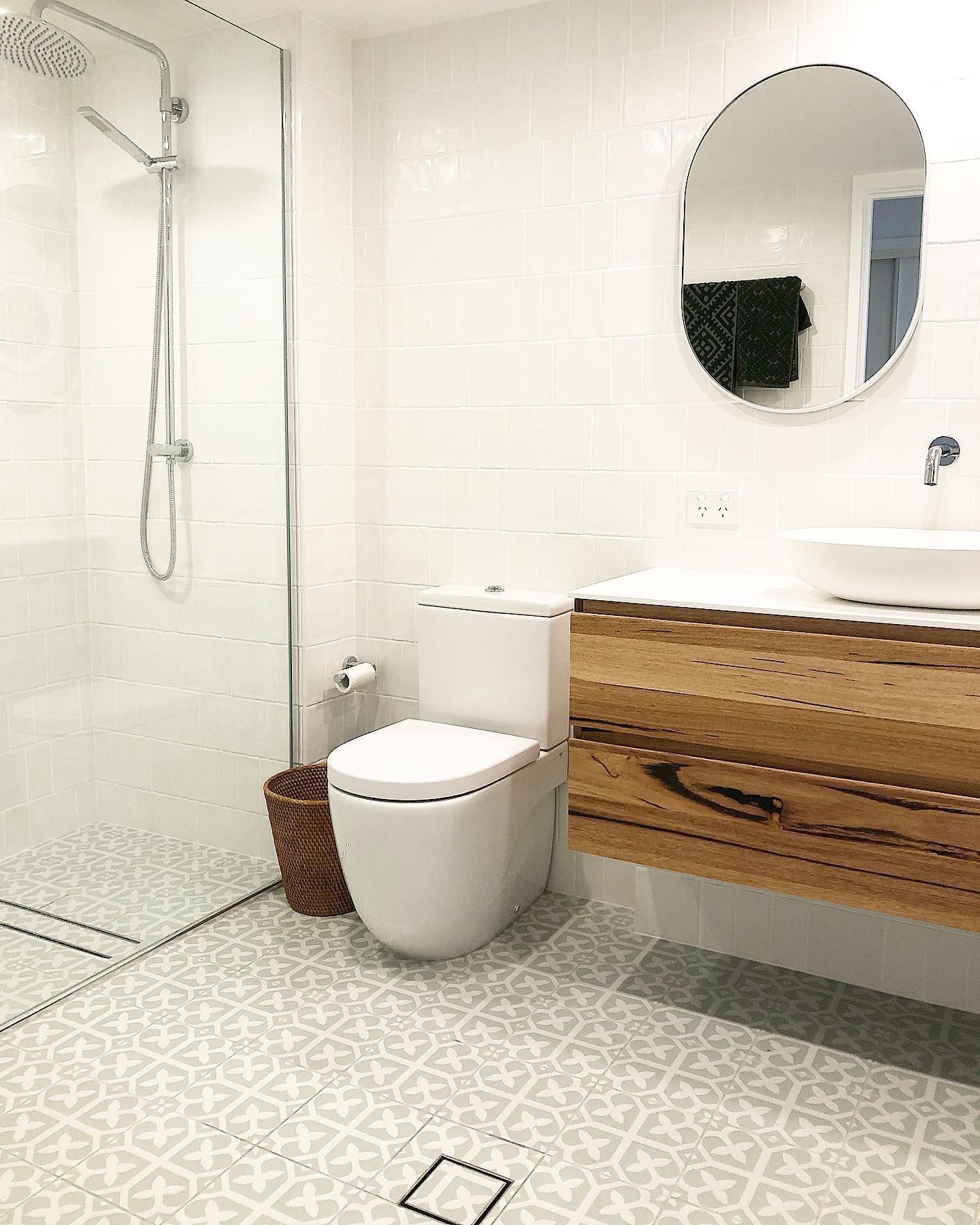 Bathroom with a white toilet, wooden vanity, oval mirror, and patterned tile floor.