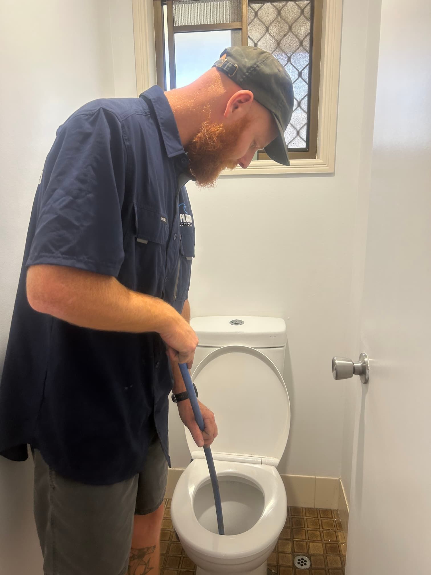 A person plunges a toilet with a black plunger, the bowl filled with water, against a gray wall.
