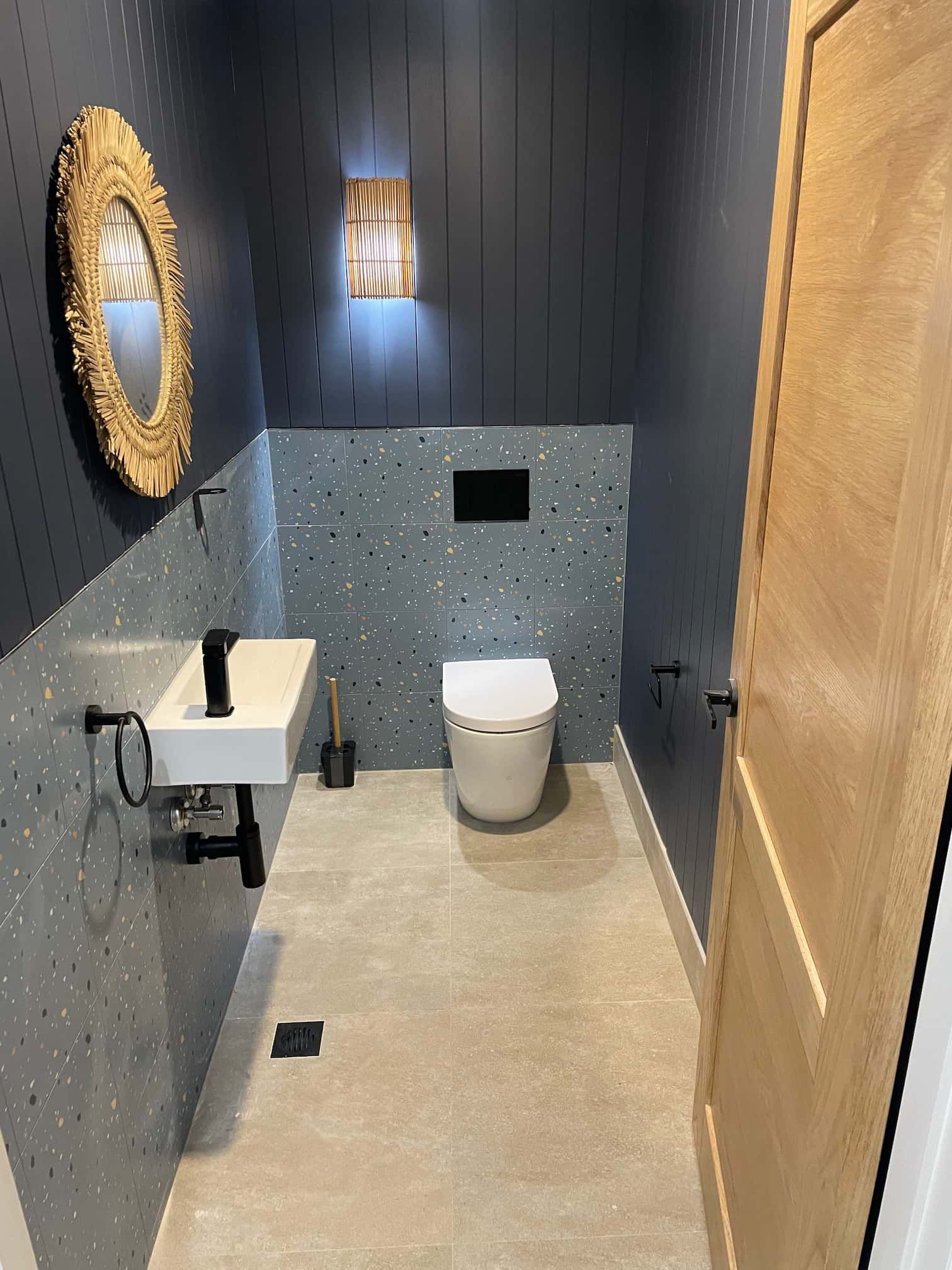 Small, modern powder room with a white toilet, sink, and decorative wall. Dark blue walls, gold mirror.