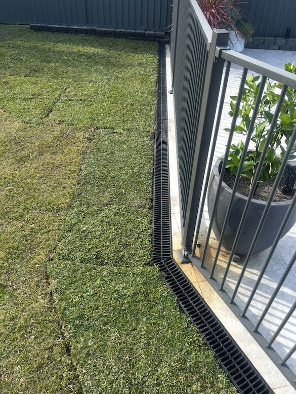 Lawn with drainage channel, beside a fence and a potted plant.