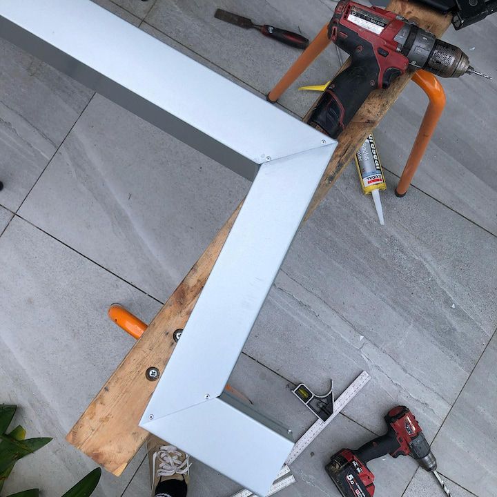 A section of light-colored metal trim in a Z shape, with tools and a wooden board on a patio.