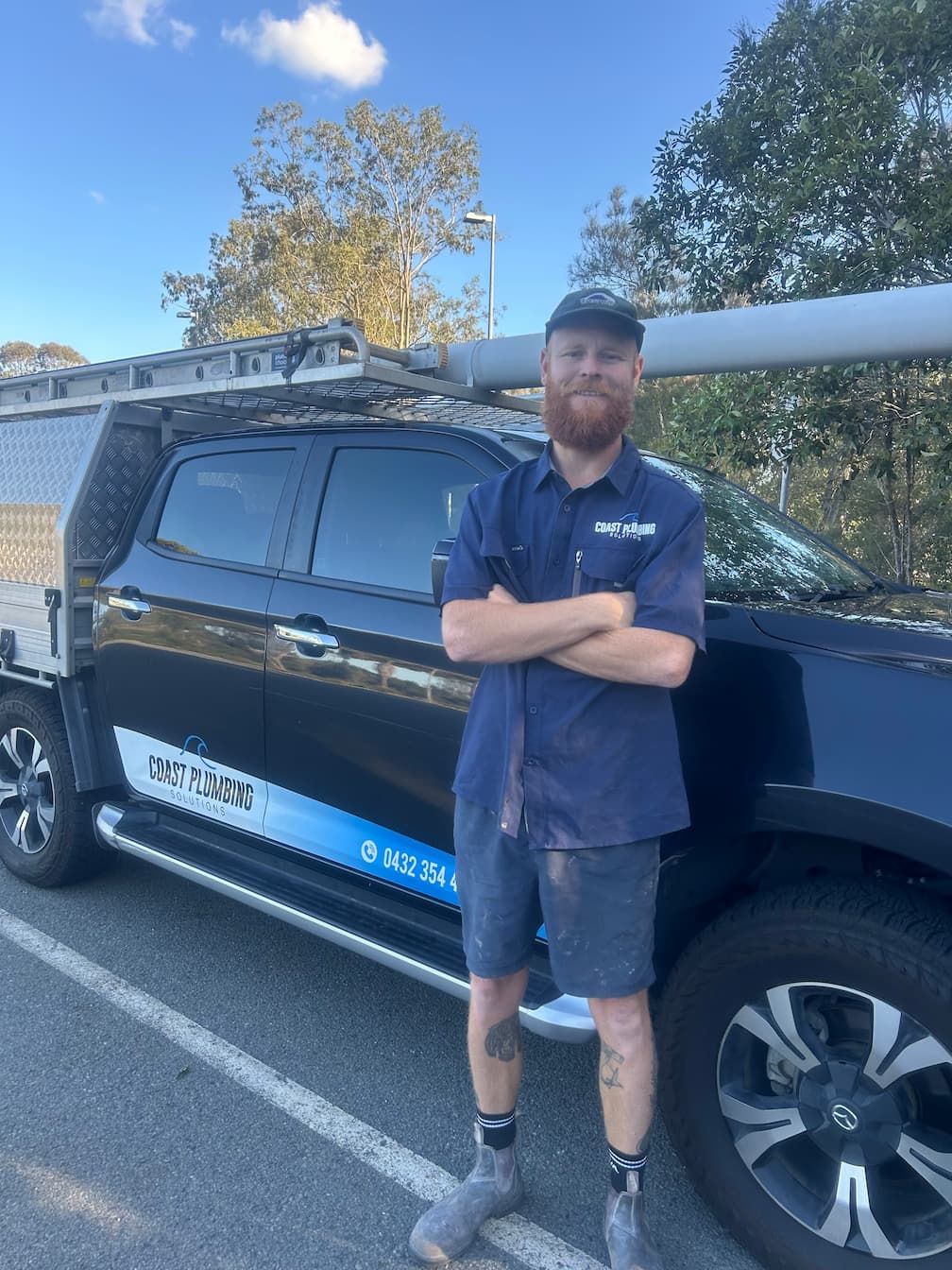 Man in work clothes standing in front of a work truck, arms crossed.