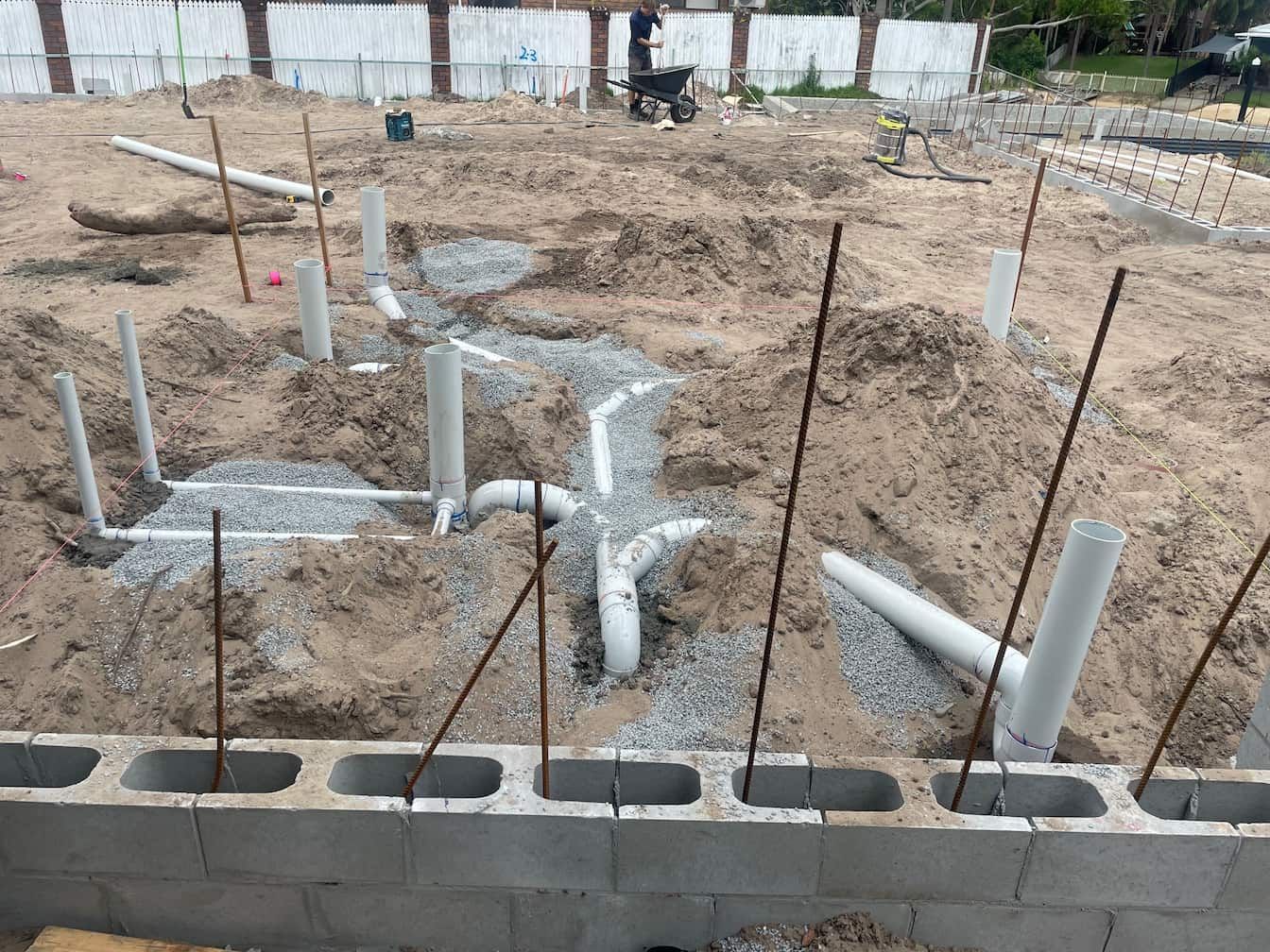 Construction site with concrete block foundation, PVC pipes for plumbing, and rebar.