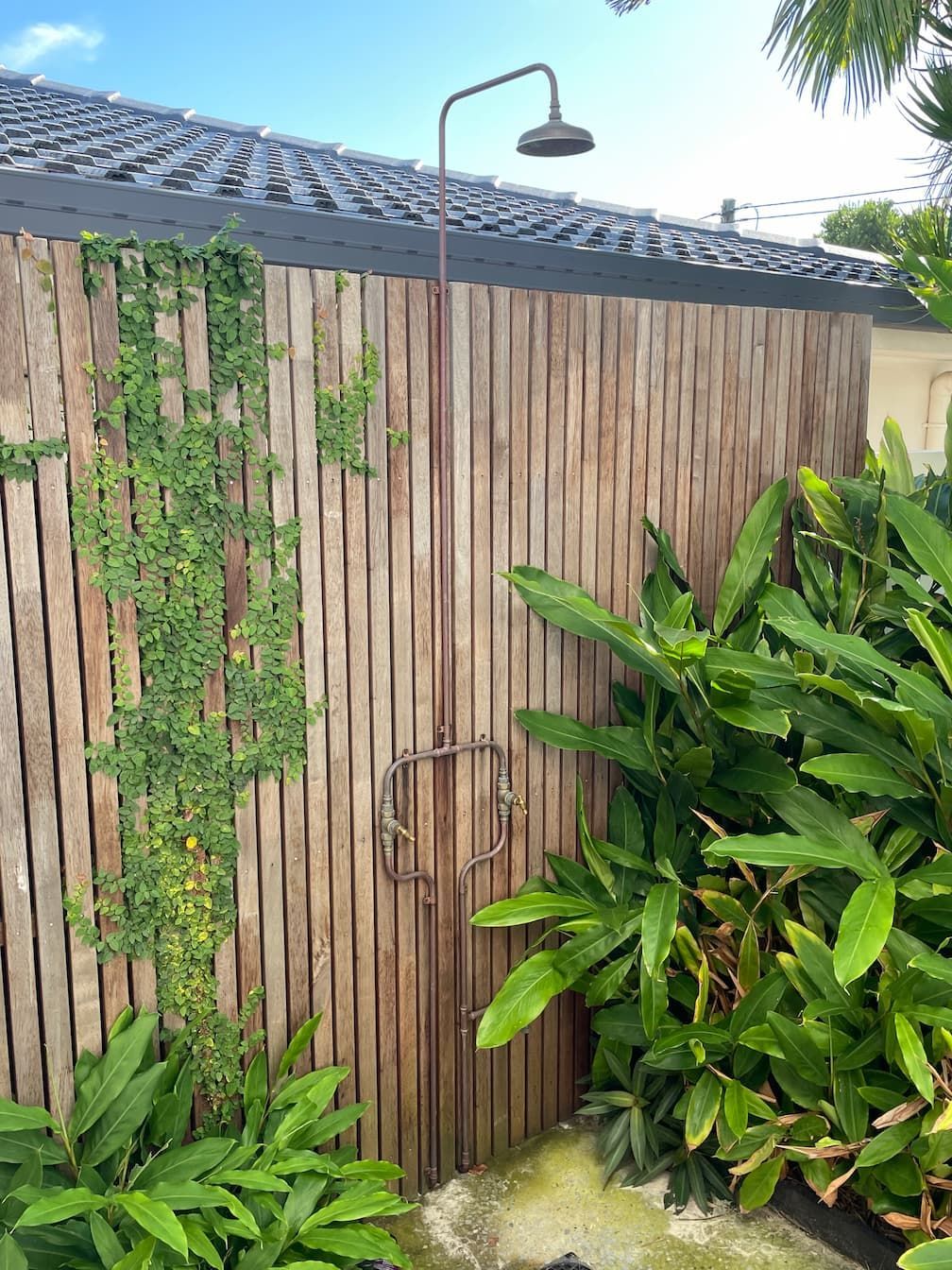 Outdoor shower head spraying water onto a white wall.