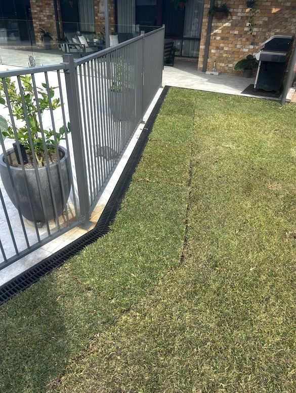A grassy backyard with a gray fence and a drainage channel.
