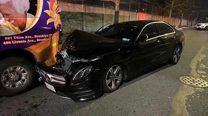 A black car is sitting next to a purple bus on the side of the road.