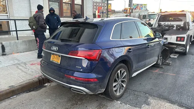 A blue car is parked on the side of the road next to a tow truck.