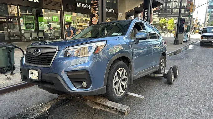 A blue suv is sitting on a tow truck on the side of the road.