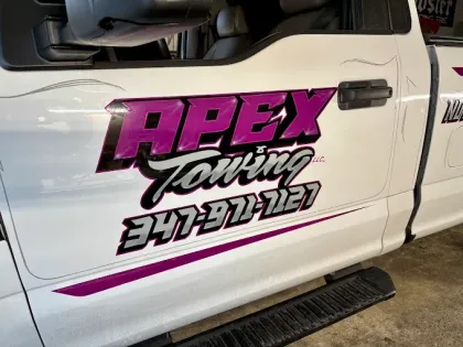 A white truck with purple and black letters that says apex towing