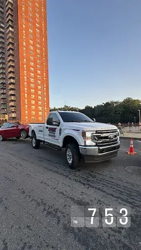 A white truck is parked on the side of the road in front of a tall building.