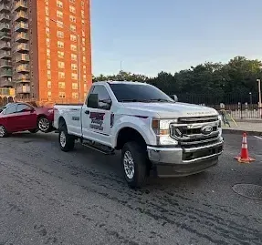 A blue car is parked on the side of the road next to a tow truck.