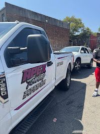 A white tow truck from Apex Towing towing a white SUV on a city street.
