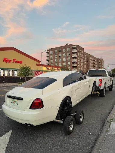 White Rolls Royce car being towed by a pickup truck on a city street.