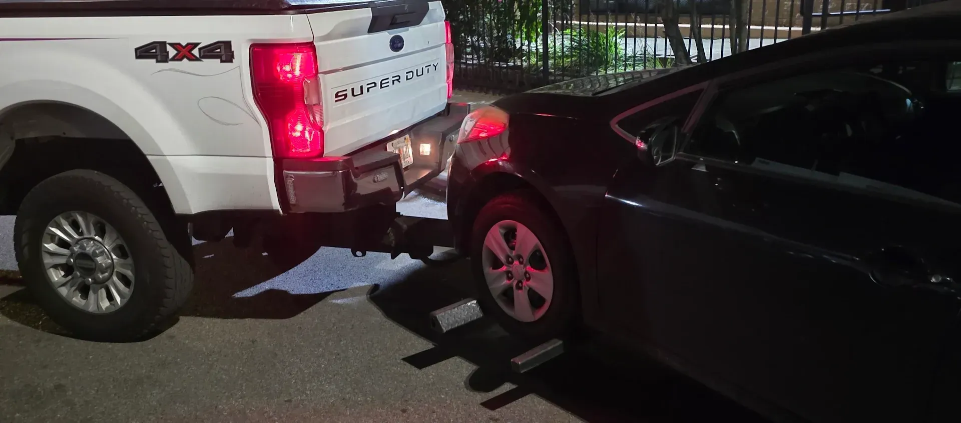 White truck backing into a black car. The truck's taillight is on. The scene is outdoors.